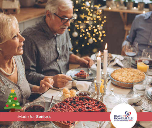 Senior couple sitting around a dinner table with candle light for Christmas dinner