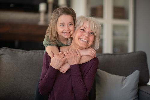 young girl giving her grandmother a hug from behind sitting on the couch