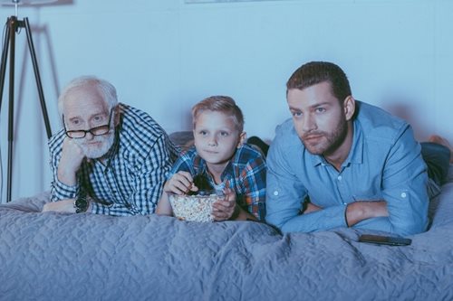 three generations of men sitting on the couch eating popcorn watching a movie
